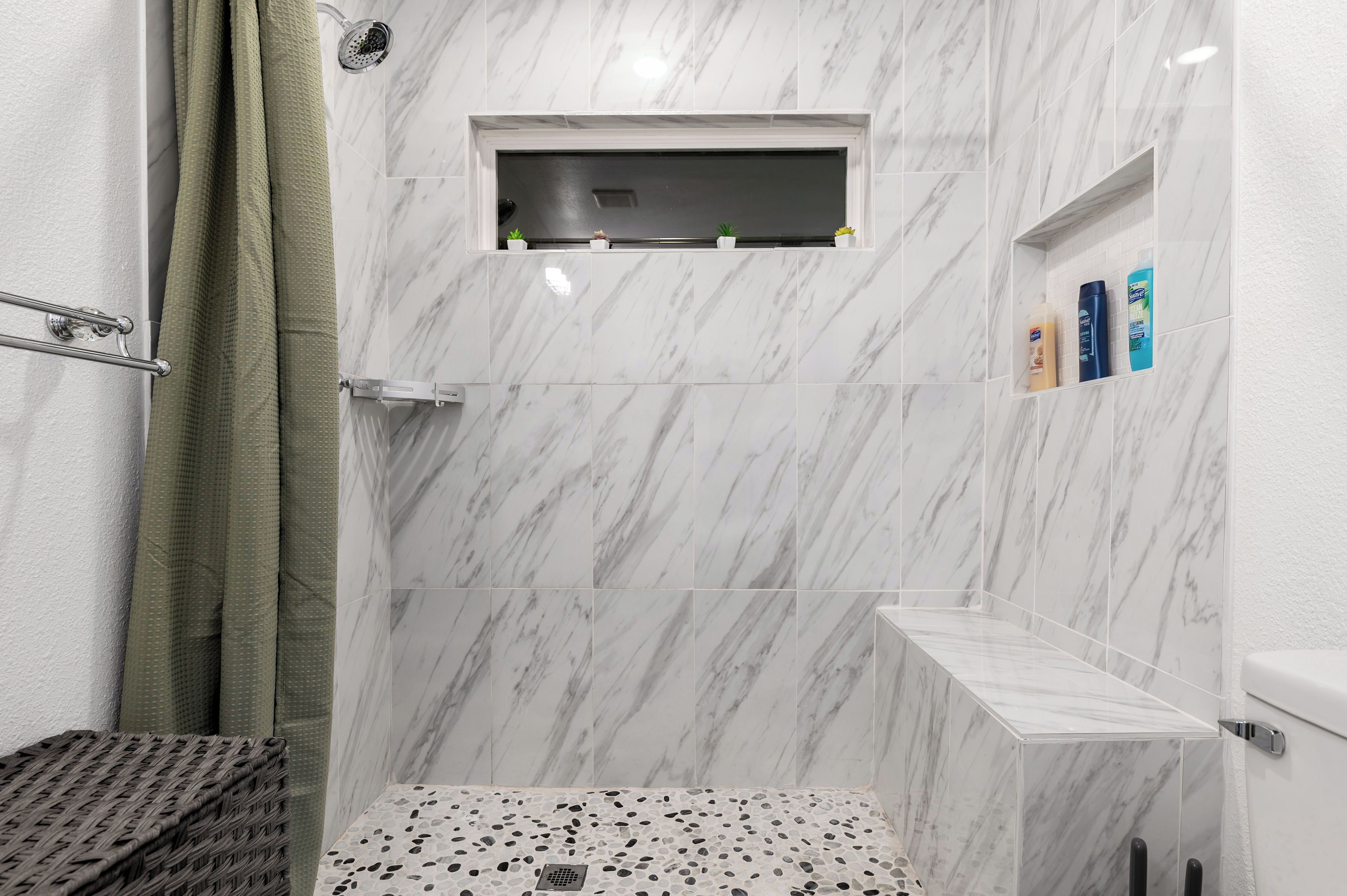 Ein Badezimmer mit Dusche, Ablage für Toilettenartikel und einem kleinen Fenster.