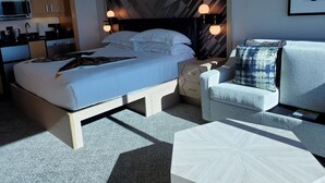 A modern hotel room with a bed, bedside tables, a sofa, a coffee table, and a kitchen area. - Elara Studio (Las Vegas)