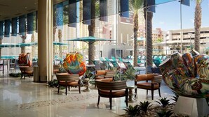 A hotel lobby with a pool area, outdoor seating, and palm trees. - Elara Studio (Las Vegas)