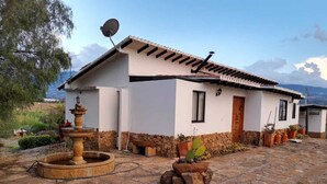 Une maison avec une terrasse en pierre, une fontaine et des plantes en pot.