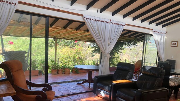Une terrasse ensoleillée avec une porte vitrée donnant sur un jardin, aménagée avec des fauteuils en cuir et une table en bois.