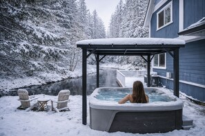 A hot tub in a snowy outdoor setting with a wooden deck and a house in the background. - Hillside Cottage: Private Pond, Hot Tub, Game Room by Hurricane Ridge, ONP (Port Angeles)
