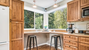 A kitchen with wooden cabinets, a white refrigerator, and a large window with a view of trees. - Hillside Cottage: Private Pond, Hot Tub, Game Room by Hurricane Ridge, ONP (Port Angeles)