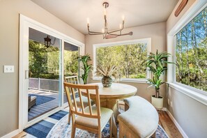 A dining area with a round table, chairs, and a chandelier. There are potted plants and a view of trees through the window. - Hillside Cottage: Private Pond, Hot Tub, Game Room by Hurricane Ridge, ONP (Port Angeles)