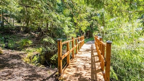 A wooden bridge with railings, surrounded by dense green foliage and trees. - Hillside Cottage: Private Pond, Hot Tub, Game Room by Hurricane Ridge, ONP (Port Angeles)