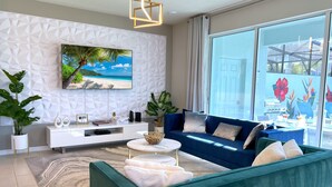 Un salon moderne avec un canapé de couleur turquoise, un meuble de rangement blanc pour les appareils électroniques et une grande fenêtre donnant sur l’extérieur.