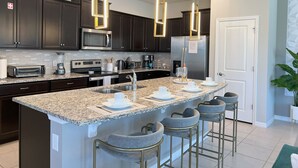 Une cuisine moderne avec des meubles de couleur sombre, des comptoirs en granit, des appareils électroménagers en acier inoxydable et un îlot central doté de tabourets de bar.
