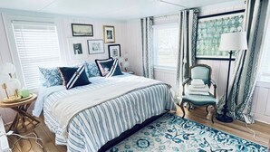 A bedroom with a large bed, a chair, a lamp, and a patterned rug.
