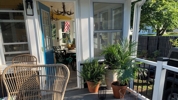 A covered porch with wicker chairs, potted plants, and a view of the backyard.