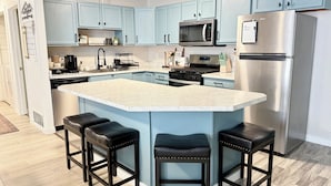 A modern kitchen with light blue cabinets, a stainless steel refrigerator, a microwave, and a central island with stools. - Restful Nest A 3bd&2ba in Midtown Anchorage (Anchorage)