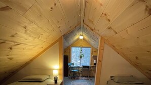 Un dormitorio acogedor en el ático con dos camas, una mesita con una lámpara y vistas al exterior a través de una ventana.
