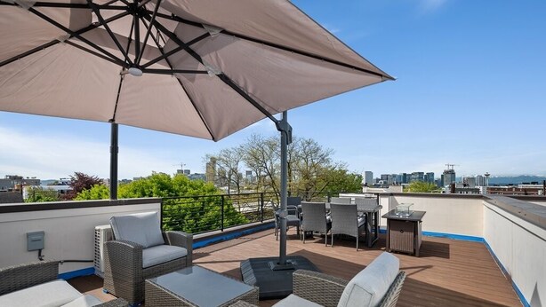 Una terraza en la azotea con mobiliario de mimbre, un paraguas grande y vistas del horizonte urbano.