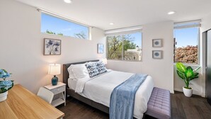 Un dormitorio moderno con cama, mesita de noche, lámpara y plantas en macetas.
