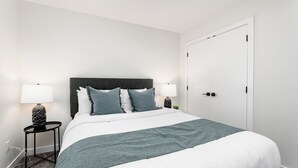 A modern hotel room with a large bed, two bedside tables with lamps, a dark headboard, and a white door. - Spruce Ave - Parking - Sleeps 4

 (Edmonton)