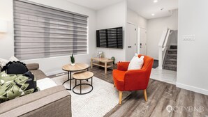 A modern living room with a sofa, a red armchair, a small table, and a TV mounted on the wall. - Spruce Ave - Parking - Sleeps 4

 (Edmonton)