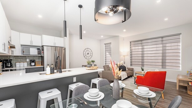 A modern kitchen with a central island, a dining area with a glass table, and a living space with a red chair and a sofa. - Spruce Ave - Parking - Sleeps 4

 (Edmonton)