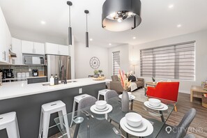 Una cocina moderna con una isla central, un comedor con mesa de vidrio y una sala de estar con una silla roja y un sofá.
