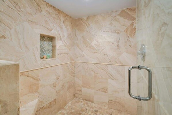 Un baño con paredes de mármol, zona de ducha y un ventanal pequeño.