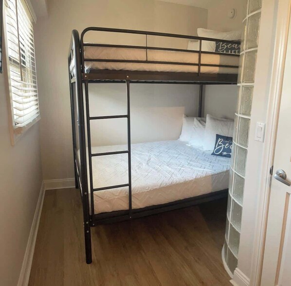 A bunk bed with a white mattress and pillows, a window with blinds, and a door with a glass panel.