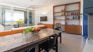 Een moderne keuken met een granieten aanrecht, een zithoek met een bank en een boekenplank vol boeken en decoratieve objecten.