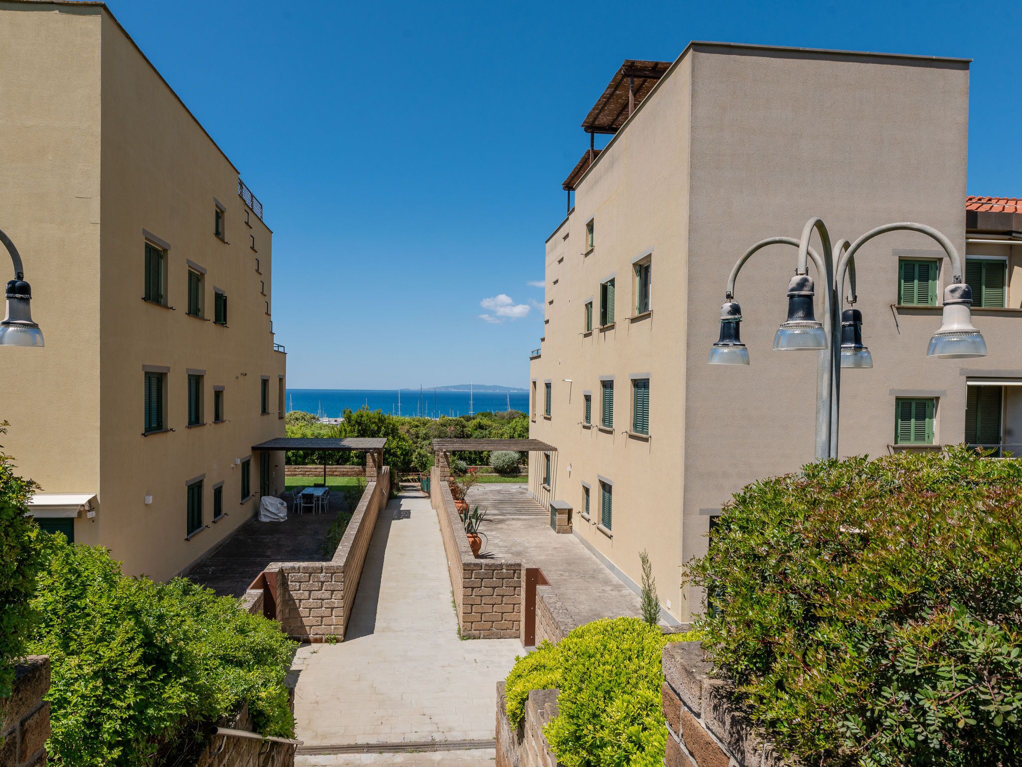 A narrow pathway between two buildings with a view of the sea.