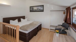 Un dormitorio con cama, escritorio, silla, ventana con cortinas y un cuadro en la pared.