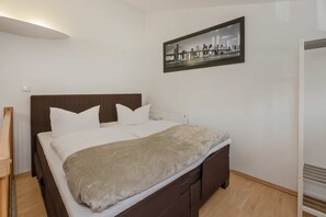Une chambre à coucher avec un lit, une tête de lit, un radiateur et un tableau représentant un paysage urbain encadré, accroché au mur.