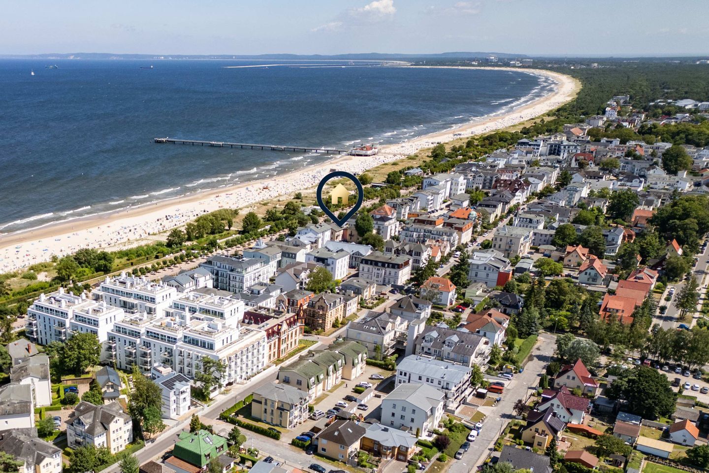 An aerial view of a coastal town with a beach, residential buildings, and a pier.