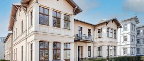Un immeuble à plusieurs étages doté d’un balcon au deuxième étage, d’une entrée bien visible et surplombant un ciel dégagé.