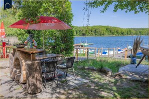 A wooden table with chairs, a red umbrella, and a view of a lake with boats.