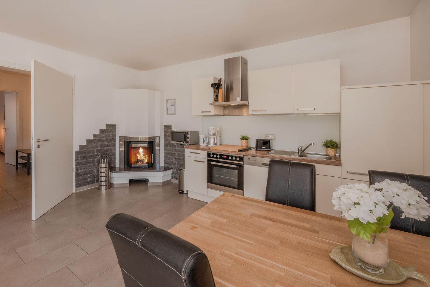 A modern kitchen with a built-in fireplace, a dining area with a table and chairs, and a kitchen island with appliances.