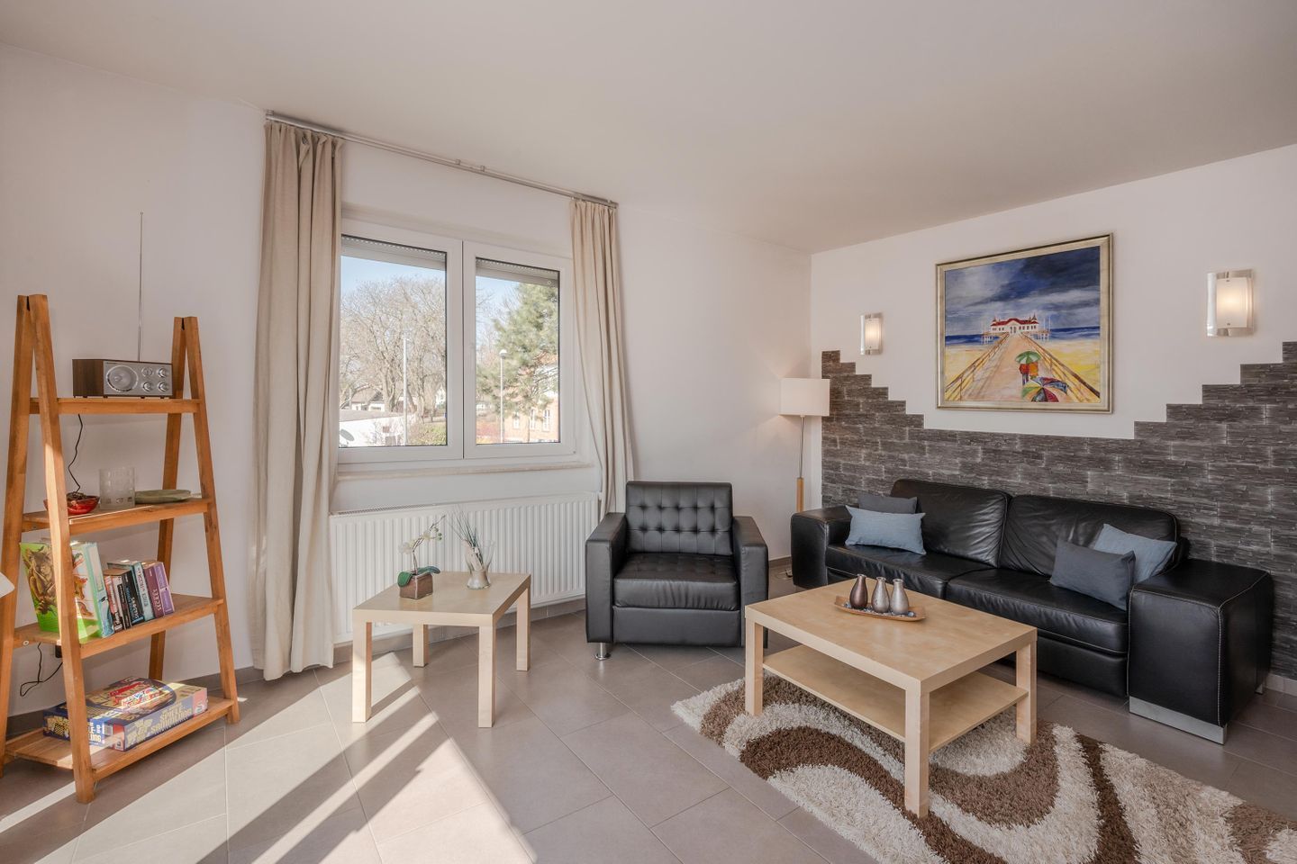 Ett vardagsrum med en soffa, en fåtölj, ett soffbord och en bokhylla.