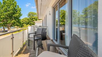 A balcony with a table and chairs, large windows, and a view of trees and a body of water.