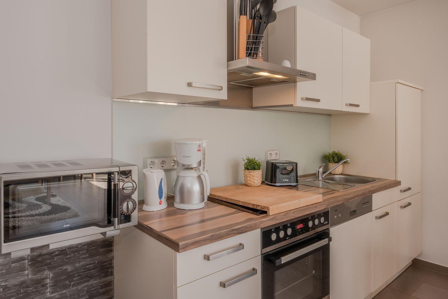 A compact kitchen with a microwave, coffee maker, toaster, and a wooden cutting board.