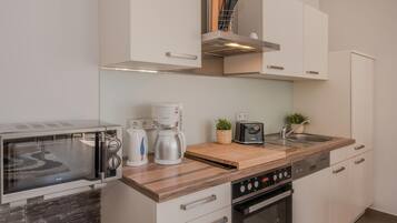 A compact kitchen with a microwave, coffee maker, toaster, and a wooden cutting board.
