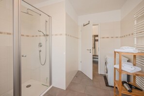 Une salle de bain moderne avec une douche à parois de verre, une étagère en bois où sont posées des serviettes et un espace buanderie bien visible.
