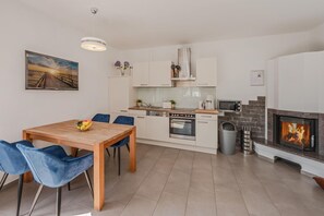 A modern kitchen with white cabinets, a wooden dining table, and blue chairs. - Komfortable, Gemütliche Fewo am Wolgastsee mit Wlan und Kamin. - Villa Petra (Korswandt)