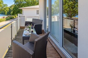 A balcony with wicker furniture, a table with wine glasses, and a view of a lake and trees. - Komfortable, Gemütliche Fewo am Wolgastsee mit Wlan und Kamin. - Villa Petra (Korswandt)