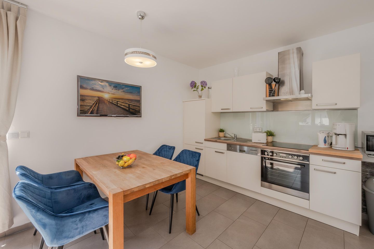 Een moderne keuken met witte kasten, een houten eettafel en blauwe stoelen.