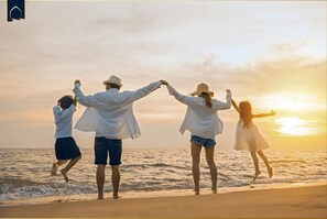 A family of four at the beach during sunset, holding hands and facing the ocean.