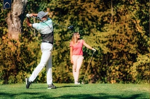 A golf course with players in motion, trees in the background, and a clear sky.