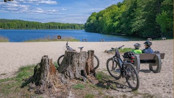 A sandy beach with bicycles, a bench, and a lake.