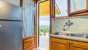 A kitchen with wooden cabinets, a stainless steel sink, and a view of a garden through an open door. - Podere la Maestà by Interhome (Rosignano Marittimo)