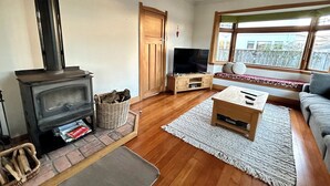 Ein gemütliches Wohnzimmer mit Kaminofen, Fernseher, Sofa und Fenster mit Blick.