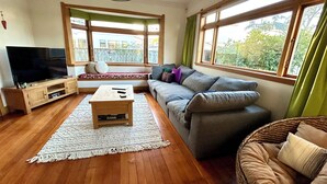 Ein Wohnzimmer mit großem Flachbildfernseher, Couch, Holztisch und Korbstuhl.