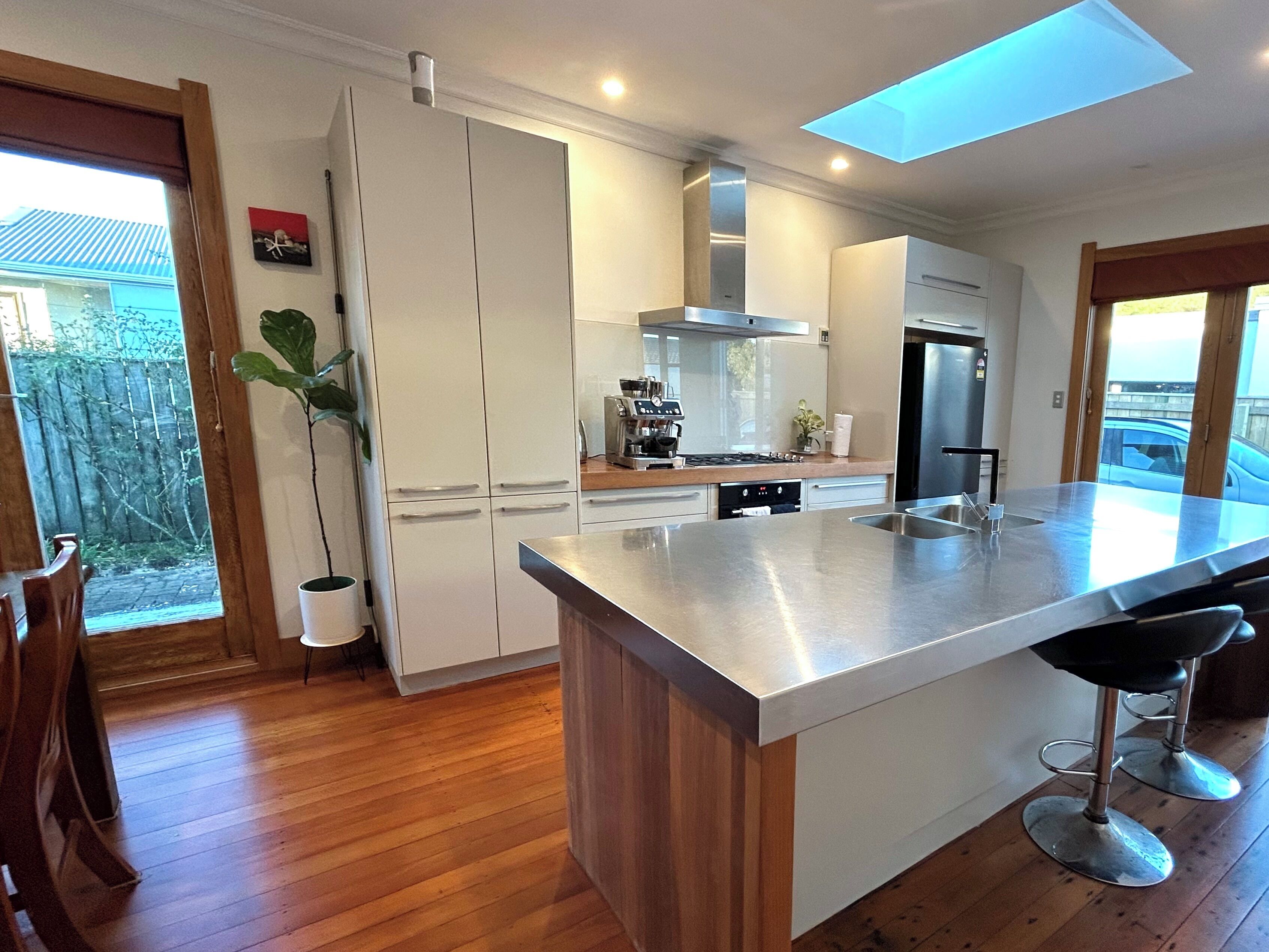 A modern kitchen with white cabinets, stainless steel appliances, a large island with bar stools, and a skylight.