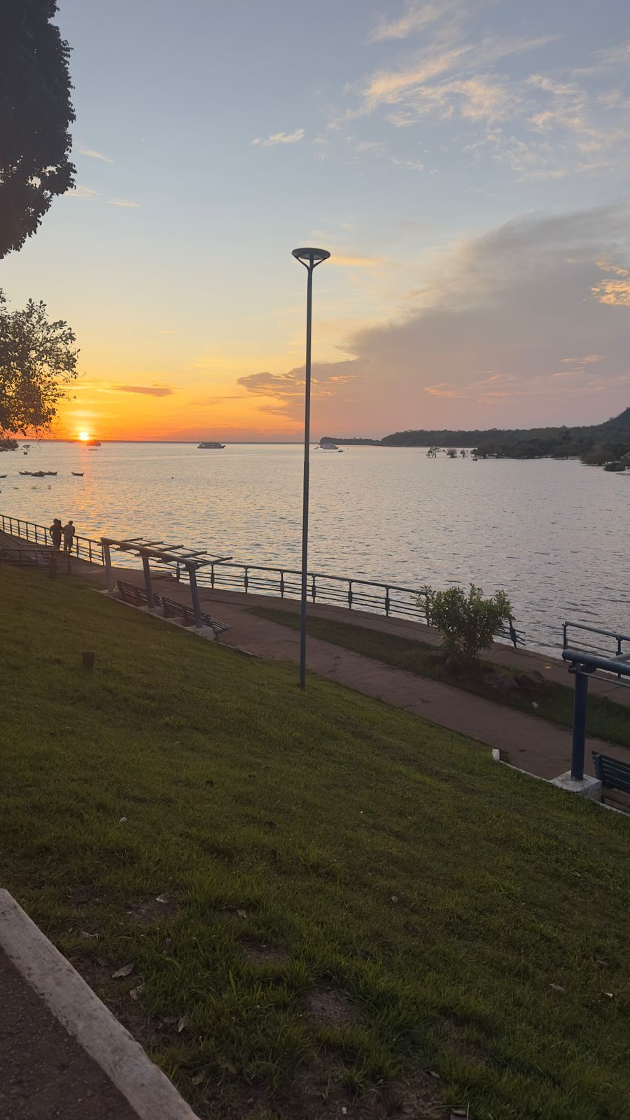 Vista del atardecer sobre una masa de agua, con un área de césped y un sendero.