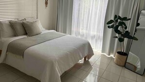 Une chambre à coucher avec un lit, des rideaux, un ventilateur de plafond et une plante en pot.