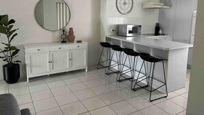Une cuisine moderne avec un plan de travail blanc, un four à micro-ondes, une horloge et un coin bar avec des tabourets.