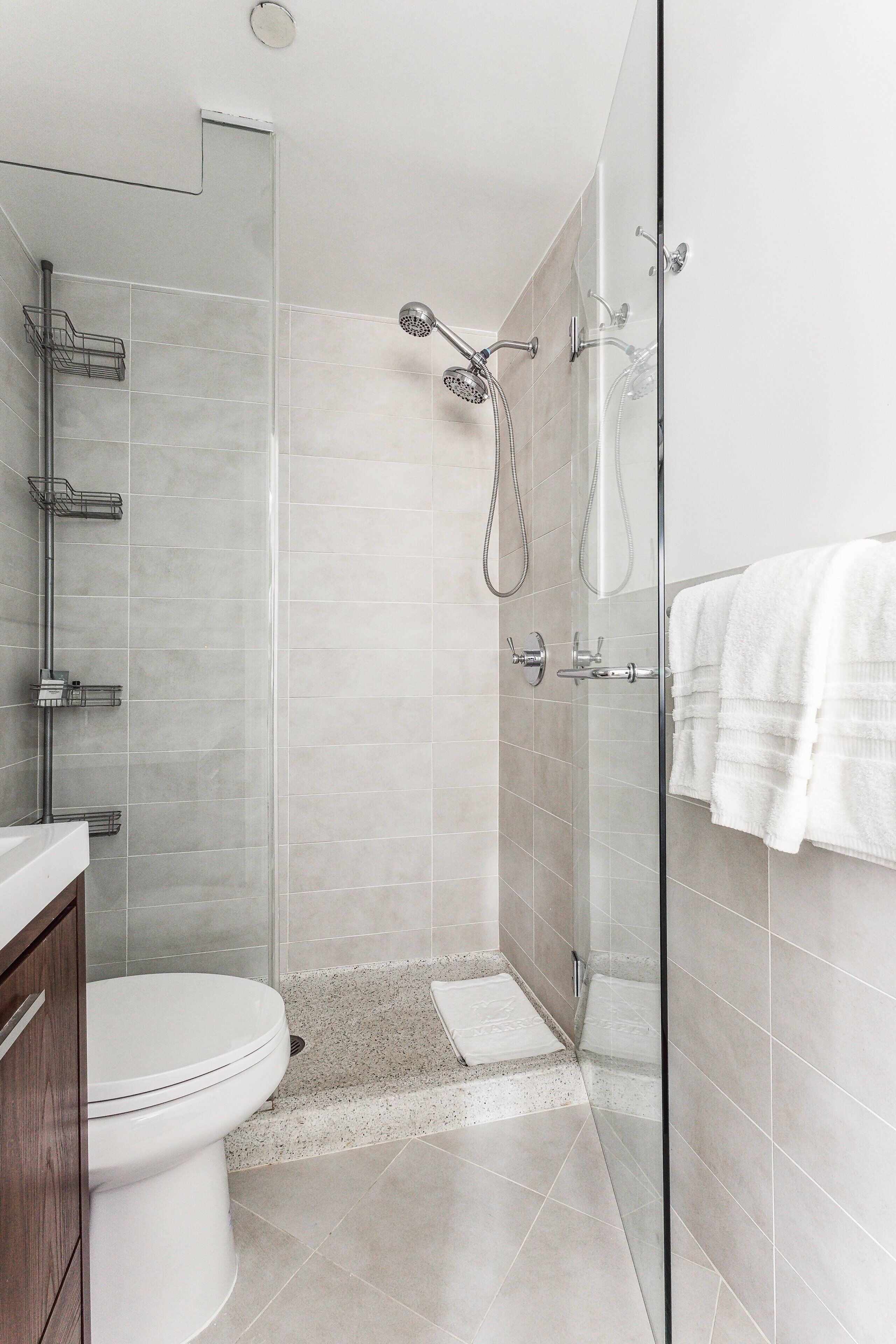 A modern bathroom with a glass shower enclosure, a toilet, and a vanity with a towel rack.